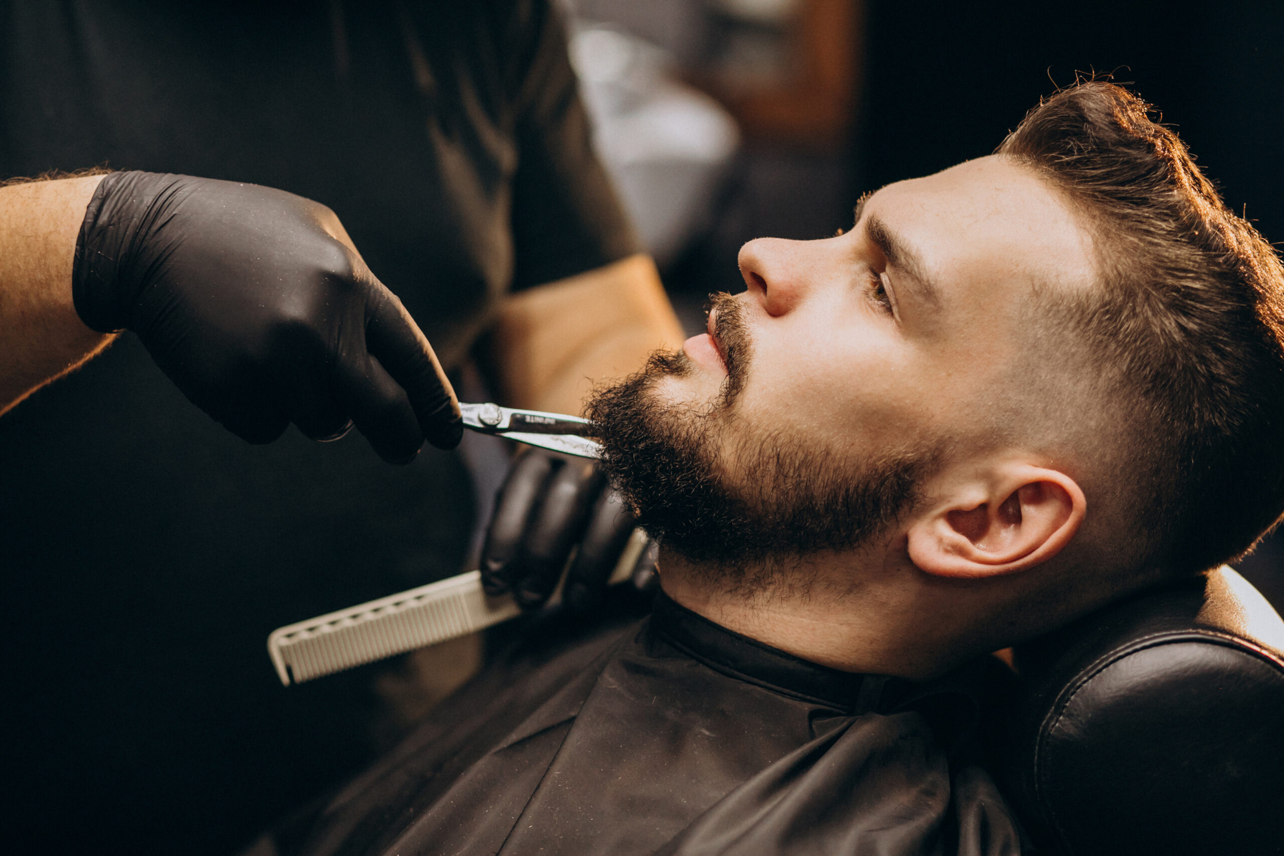 Handsome man cutting beard at a barber shop salon